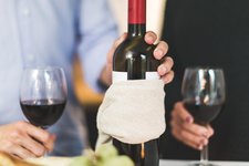 man holding white labeled red wine bottle near wine glasses
